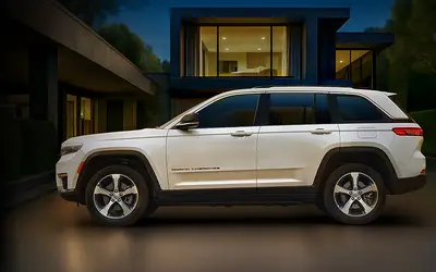 Jeep Grand Cherokee side profile in white outside a modern house at dusk