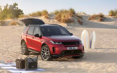 Land Rover Discovery Sport in red with the tailgate open on a coastal dune