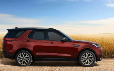 Land Rover Discovery side profile in red beside a wheat field