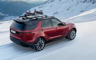 Land Rover Discovery rear three-quarter view in red on a snow-covered road with a roof rack