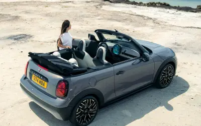 MINI Cooper Convertible in grey with the roof down by the sea, rear three-quarter view