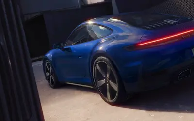 Porsche 911 Carrera rear three-quarter view in blue, showing the full-width tail light bar