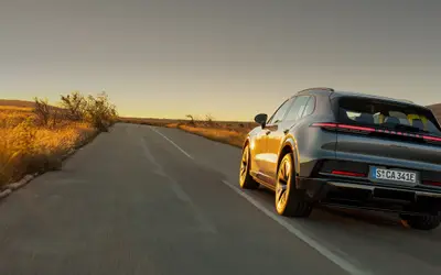 Porsche Cayenne Electric with gold wheels driving away on an open road, rear three-quarter view