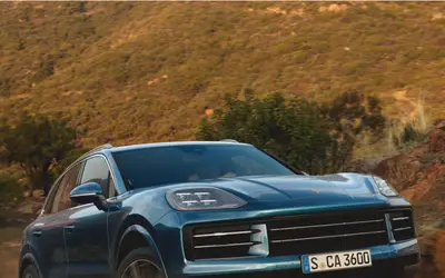 Porsche Cayenne in teal blue on a hillside road, front three-quarter view
