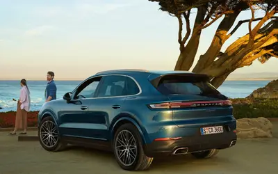 Porsche Cayenne in teal blue with the tailgate open at the coast, rear three-quarter view