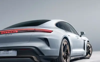Porsche Taycan Turbo S rear three-quarter studio view in white, showing the full-width light bar