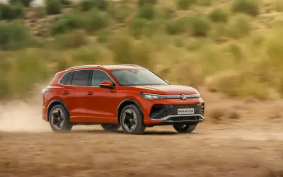 Volkswagen Tiguan R-Line side view in orange-red, driving on a dirt trail